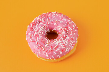 Fototapeta na wymiar pink glazed donut with confectionery sprinkles on an orange background close-up