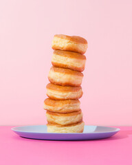 Donuts stuck on top of each other. Pink background. Unhealthy eating concept.