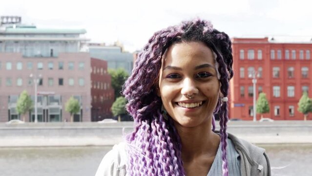 portrait of a modern african american woman outdoor, stylish black girl with purple curls on the river bank in the city
