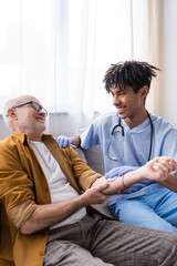 Smiling african american nurse holding cotton pad on hand of senior patient at home.