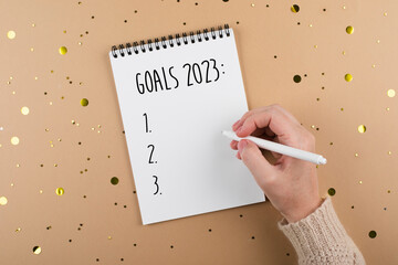 New Year goals 2023. Woman's hand writing in note pad goals list. Concept of new year planning