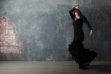 Fototapeta premium Young adult spanish woman dancing flamenco on gray vintage studio background