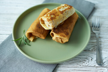 Stuffed pancakes with apples on a green plate decorated with a sprig of rosemary and a fork.