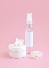 Fototapeta na wymiar White cosmetic jar and bottle near white orchid flowers on light pink close up. Package Mockup