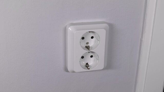 A man unplugging a cord from a wall socket, to help save energy and the environment. Static close up shot.