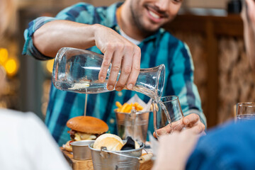 food, leisure and people concept - happy smiling man having dinner at restaurant and pouring water from jug to glass