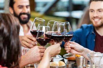 leisure, people and celebration concept - close up of happy friends drinking red wine and toasting at restaurant or pub