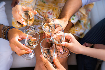 Group of friends toasting together - detail on hands clinking champagne flutes - event, birthday, anniversary or celebration lifestyle concept - focus on the left hand