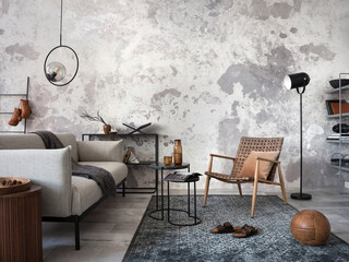 Loft style of modern apartment with grey design sofa, mock up paintings, black coffee table, black ladder, pedant lamp, carpet, decoration and elegant accessories . Concrete grunge wall. Template.