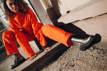 Young brunette curly woman in orange suit. Female in colorful overalls portrait