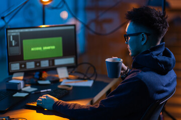 cybercrime, hacking and technology concept - male hacker in dark room drinking coffee and using...