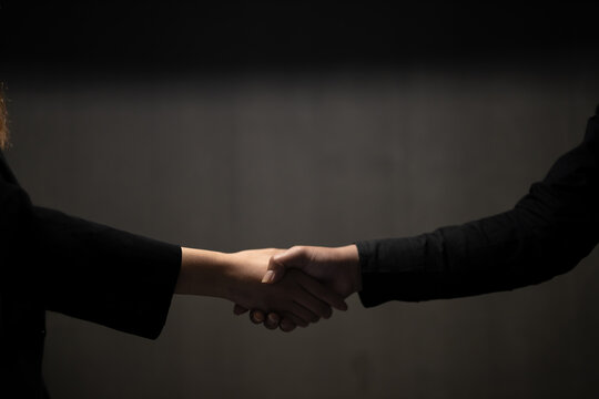 Anonymous business partners making handshake in dark shadow