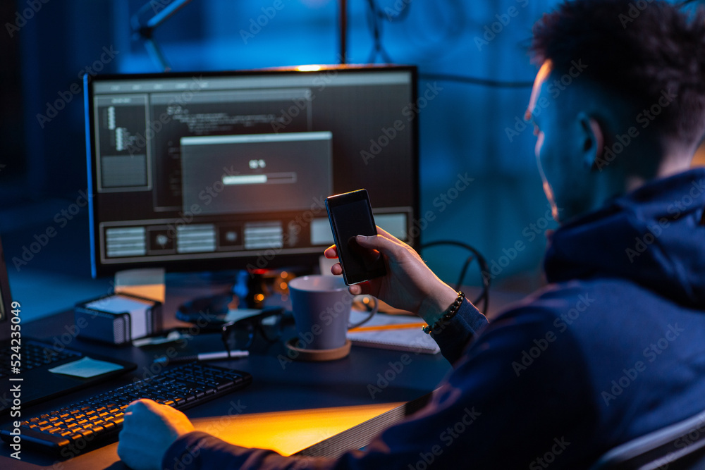 Poster cybercrime, hacking and technology concept - close up of male hacker with smartphone using computer 