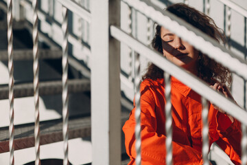 Young brunette curly woman in orange suit. Female in colorful overalls portrait