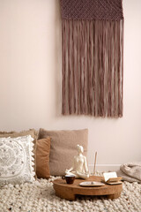 Boho and cozy interior of meditation space with a lot of pillows, plaid, hanging macrame, wooden tray with accessories, decoration, carpet and personal stuff. Warm and minimalist home decor. Template.