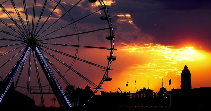Ferris Wheel and illuminations in amusement park during  scenic sunset with dramatic sky clouds and flying birds