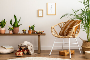 Creative composition of elegant and boho living room with wooden armchair, a lot of plants, cacti, books, baskets, mock up photo frames, carpet and personal accessories. Cozy home decor. Template.
