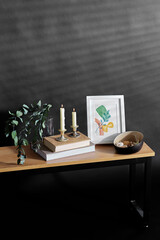 interior and home decor concept - bench with burning candles, picture in frame, books, sea shells and eucalyptus branches over black background