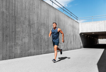 fitness, sport and healthy lifestyle concept - young man running out of tunnel