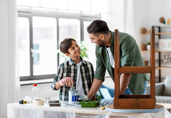 repair, diy and home improvement concept - happy smiling father and son in protective gloves stirring grey color paint in can for painting old wooden table
