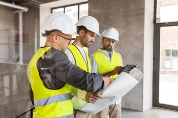 architecture, construction business and people concept - male architects in helmets with blueprint and tablet pc computer working in office building