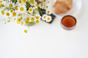 Top view of a tea with fresh sweet croissants on the table with a vase of daisies. In the middle of the table is a smartphone. Sunday breakfast in backyard of a cottage. Copy space. High quality photo