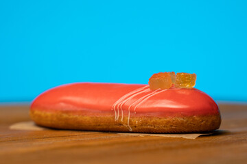 sweet eclair with orange glaze on a wooden table on a blue background. 
