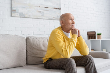 Grey haired man sitting on couch in living room.