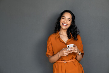 Laughing happy smiling woman messaging on mobile phone on gray wall