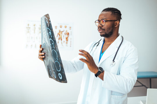 Young doctor looking at computed tomography x-ray image. Confident pleasant doctor working with MRI scan results. Radiologist man checking x-ray, health care, medical and radiology concept
