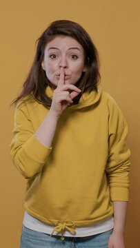 Portrait of woman being scared doing hand gesture touching face in fear feeling frightened and afraid over yellow background. Young person doing shocked face grimace being startled in studio.