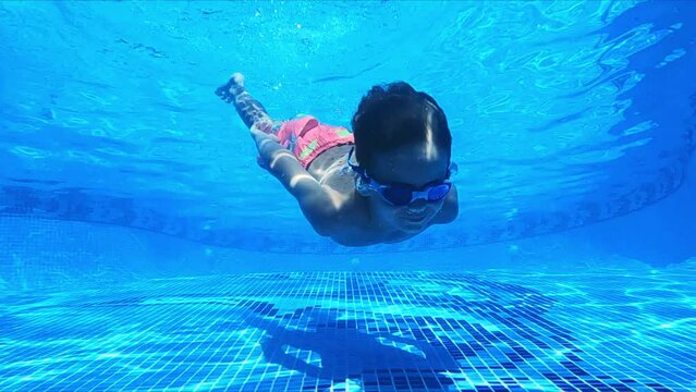  Funny boy swimming underwater in blue clean pool. Children freediving 