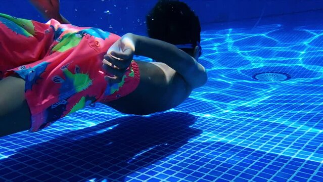 Funny little boy swimming underwater in clean blue pool. Children freediving