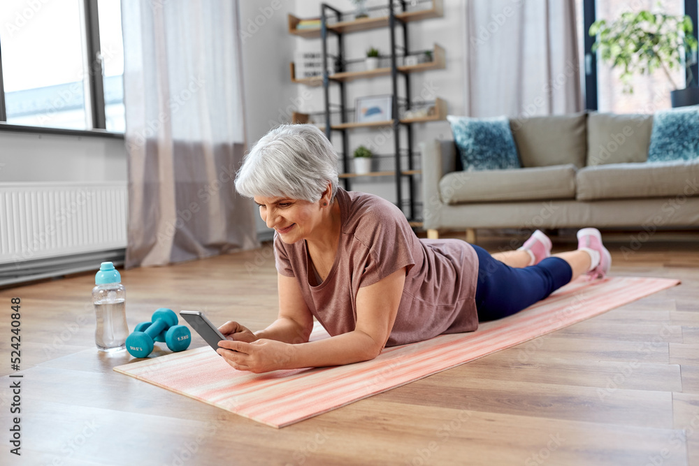 Wall mural sport, fitness and healthy lifestyle concept - smiling senior woman with smartphone exercising on ma