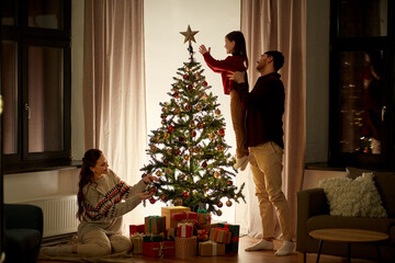 family, winter holidays and people concept - happy mother, father and little daughter decorating christmas tree at home