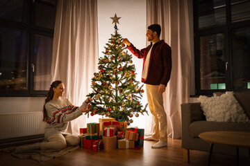 winter holidays and people concept - happy couple decorating christmas tree at home - Powered by Adobe