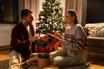 holidays, celebration and people concept - happy couple opening christmas gifts at home