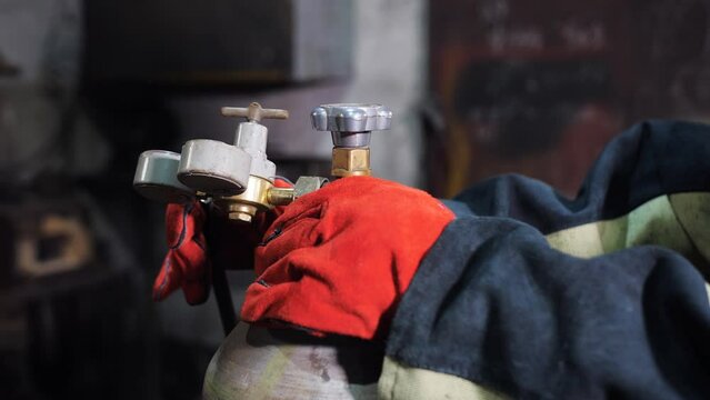 Close-up of hands a male welder in red work gloves unscrews a valve on a gas cylinder for argon welding.