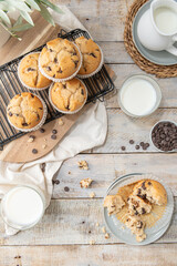 Chocolate chip muffins on a baking rack and glasses of milk on a white kitchen countertop.  Morning breakfast table. Top view, flat lay