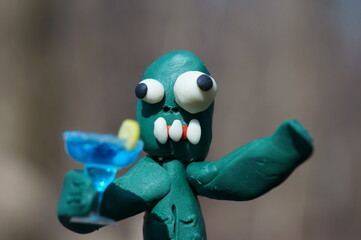 A toy zombie with a funny face holds a cocktail glass in his hand.