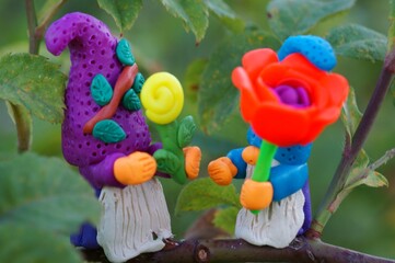 Figures of dwarfs with flowers on a tree branch. Fabulous toys made of plasticine.