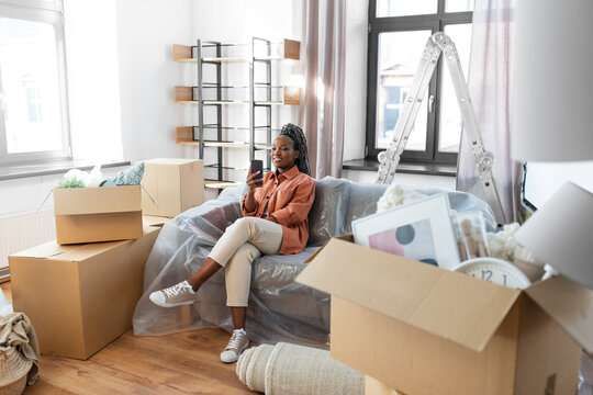 people, repair and real estate concept - woman with smartphone and boxes moving to new home