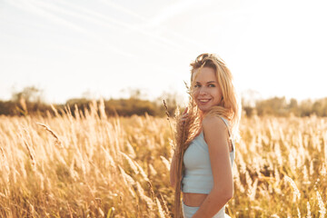 Beautiful blonde woman on a walk in a field with dry grass. A walk in nature, sunset in a field of...