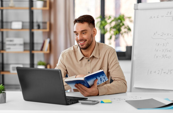 Distant Education, School And Remote Job Concept - Happy Smiling Male Math Teacher With Laptop Computer, Book And Flip Chart Having Online Class Or Video Call At Home Office