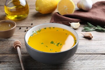 Bowl with lemon sauce and ingredients on wooden table. Delicious salad dressing