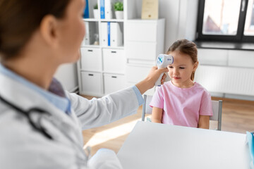 medicine, healthcare and pediatry concept - female doctor or pediatrician measuring little girl patient's temperature with infrared forehead thermometer at clinic