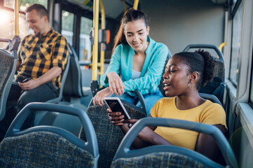 Multiracial group of friends talking while riding in a bus and using a smartphone