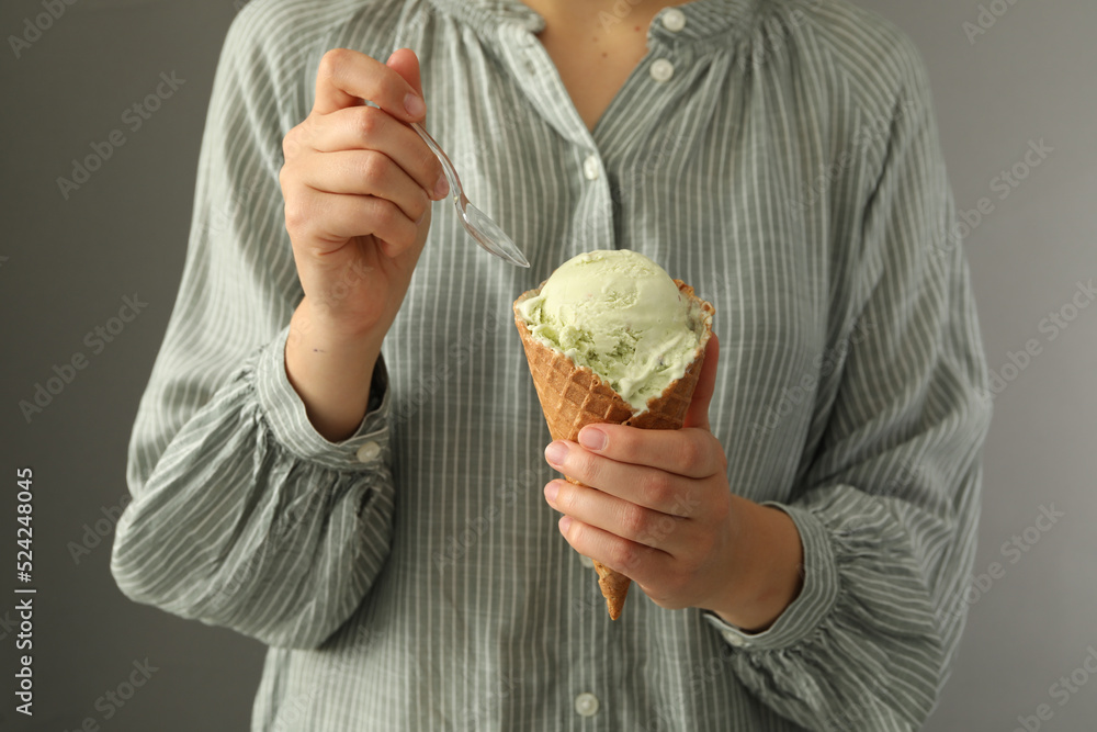 Wall mural woman eating green ice cream in wafer cone on grey background, closeup