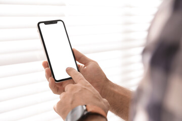 Man using mobile phone with empty screen near window indoors, closeup