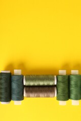 Different shades of green sewing threads on yellow background, flat lay. Space for text